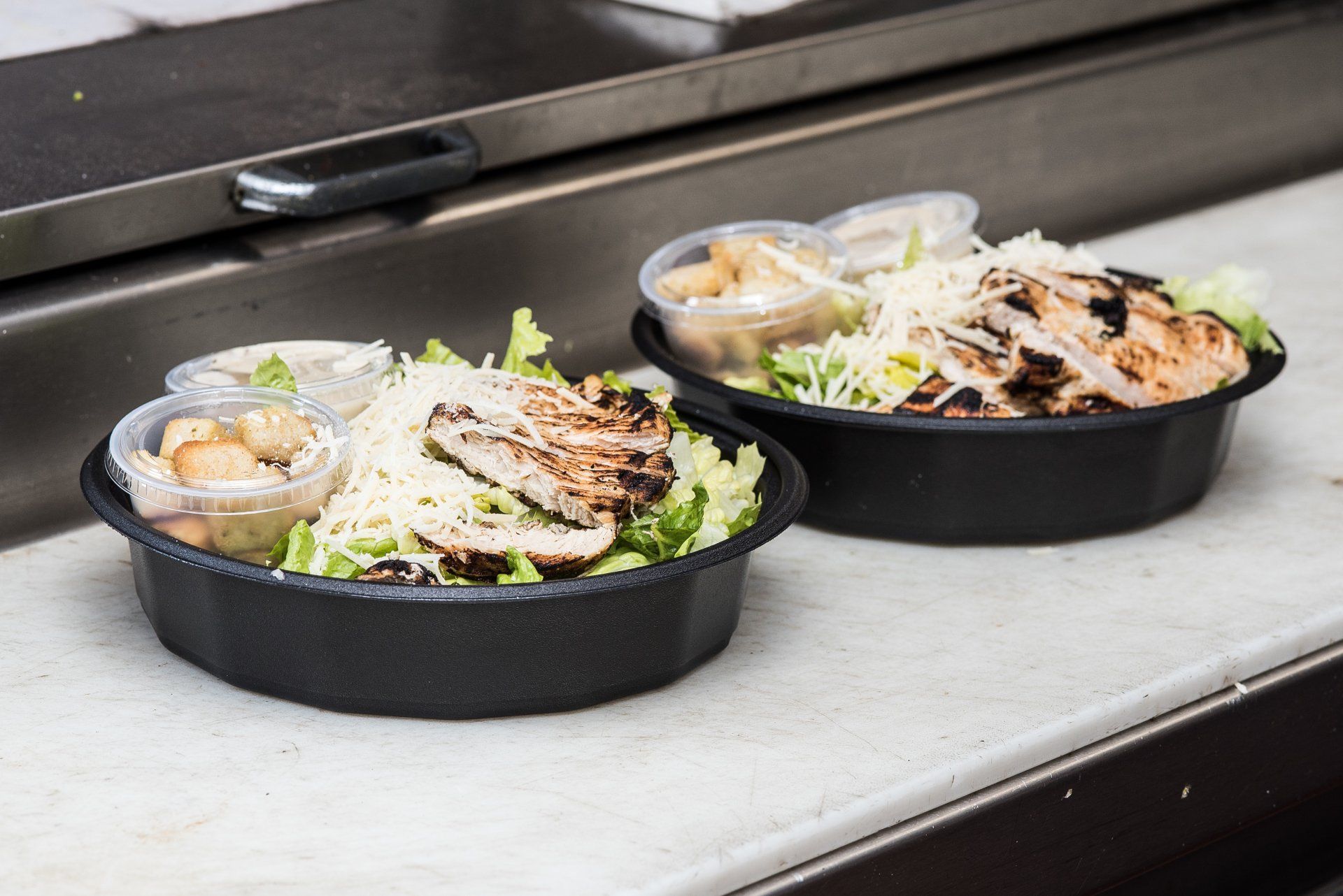 Grilled chicken Caesar salads packed in carry-out bowls on the kitchen counter